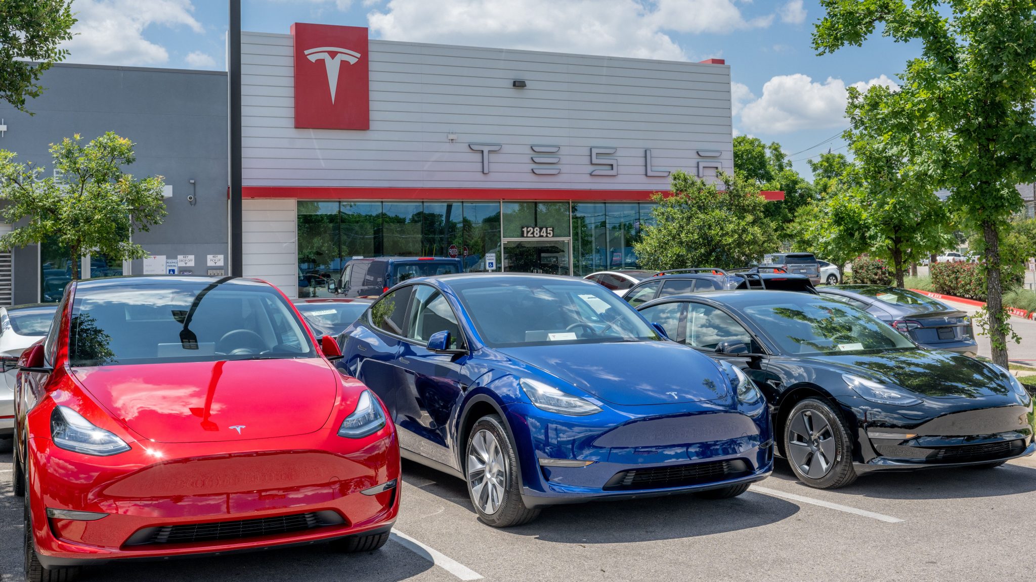 Image showing several Tesla Model 3 sedans parked outside a Tesla Sales Centre.